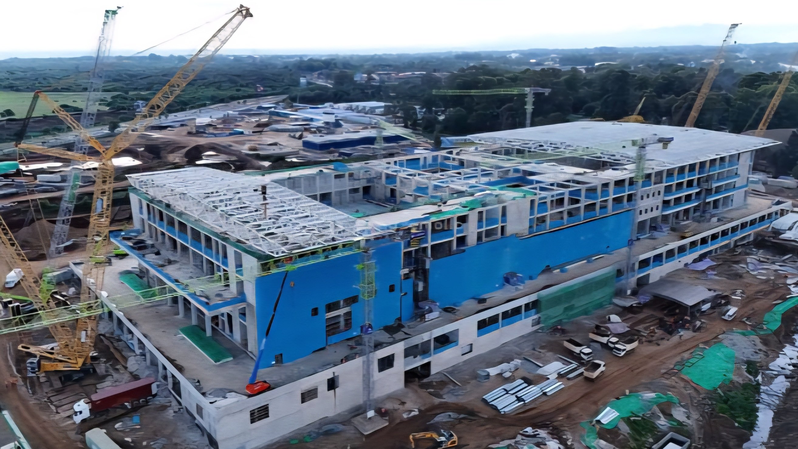 A construction site view of the Bomas International Convention Complex showing structural steel framing for the roof, concrete pillars, and heavy machinery, with engineers reviewing project plans in the foreground.