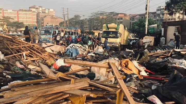 An excavator clearing debris from demolished wooden and metal kiosks along a roadside in Roysambu, Nairobi.