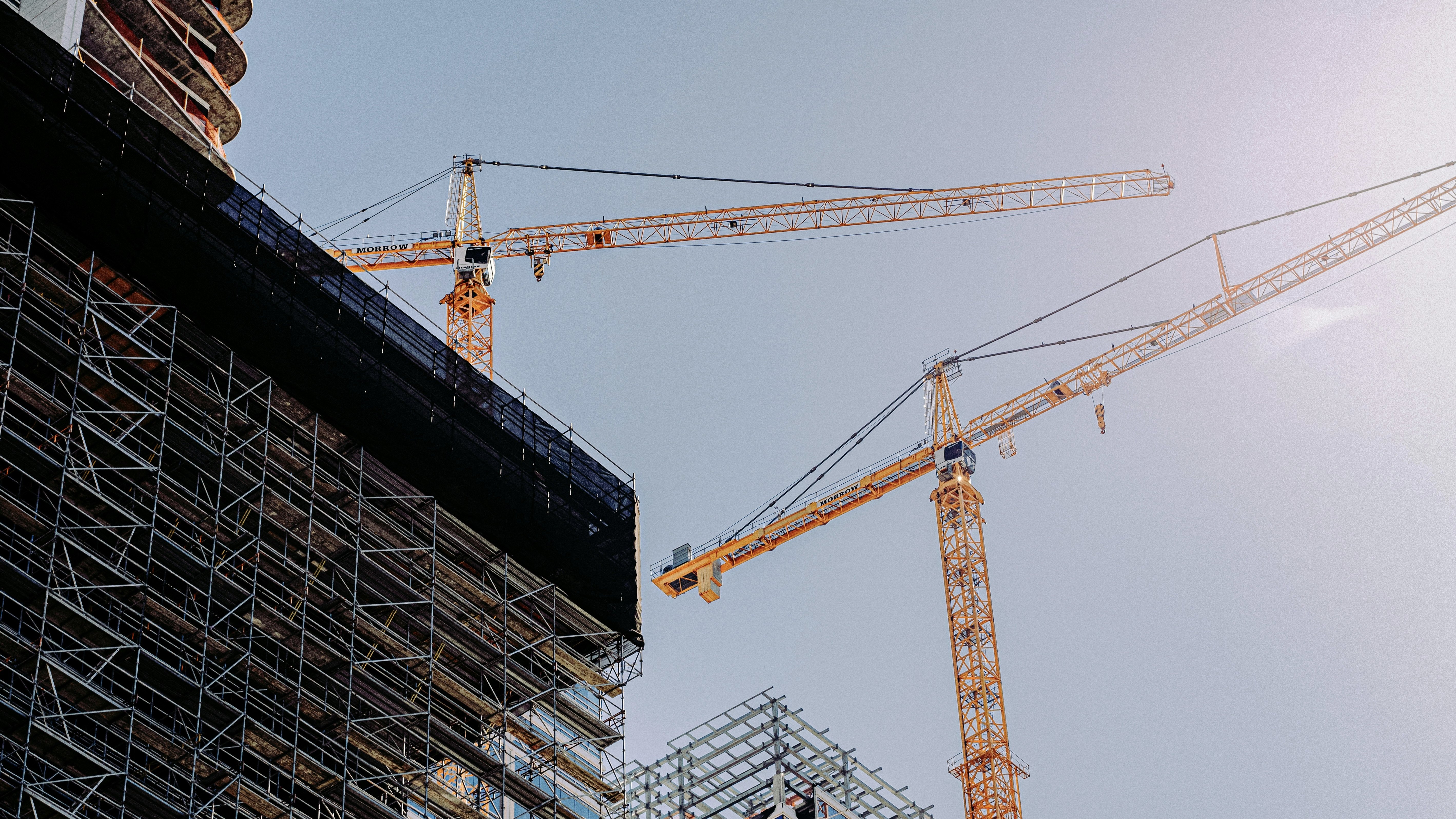Large scale construction site with multiple yellow cranes and concrete foundations of a major infrastructure project under a hazy sky.