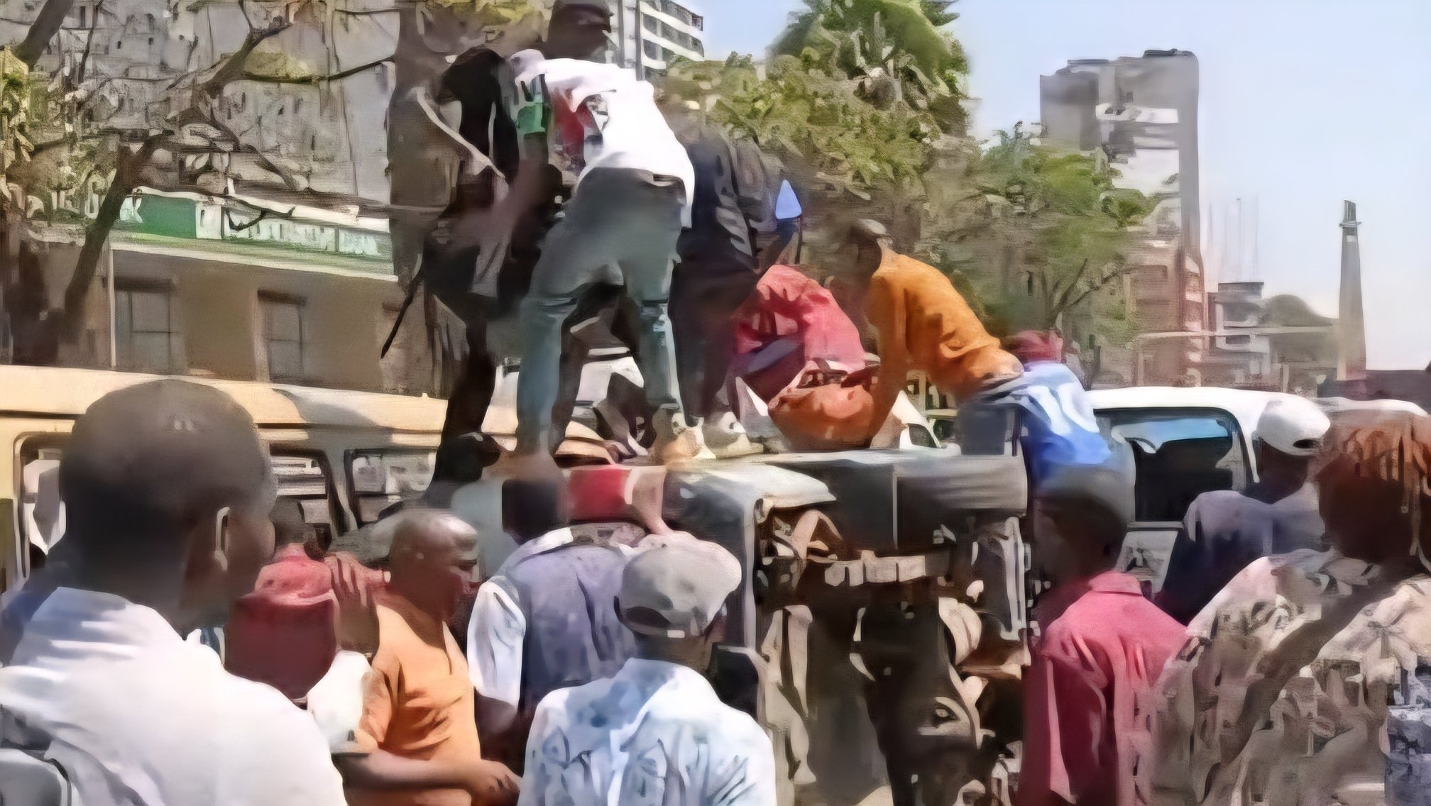 A white and yellow public service matatu lying on its side across two lanes of a busy urban road with police and emergency responders nearby.