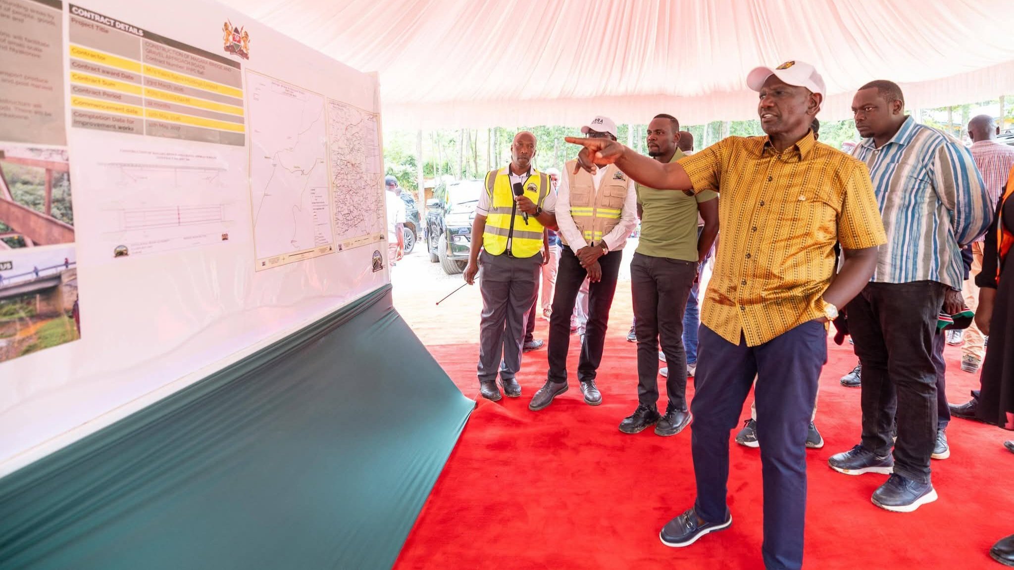 President William Ruto points at a project map under a white tent while surrounded by officials during the road launch in Kisii.
