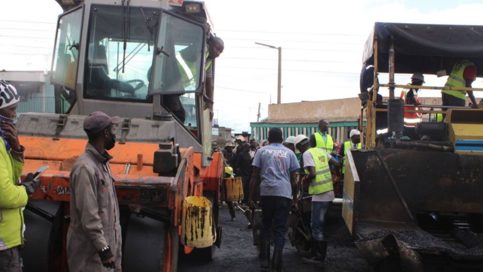Heavy engineering machinery, including an asphalt roller, operating on a newly paved road during the infrastructure upgrade works in Huruma, Ol Kalou.