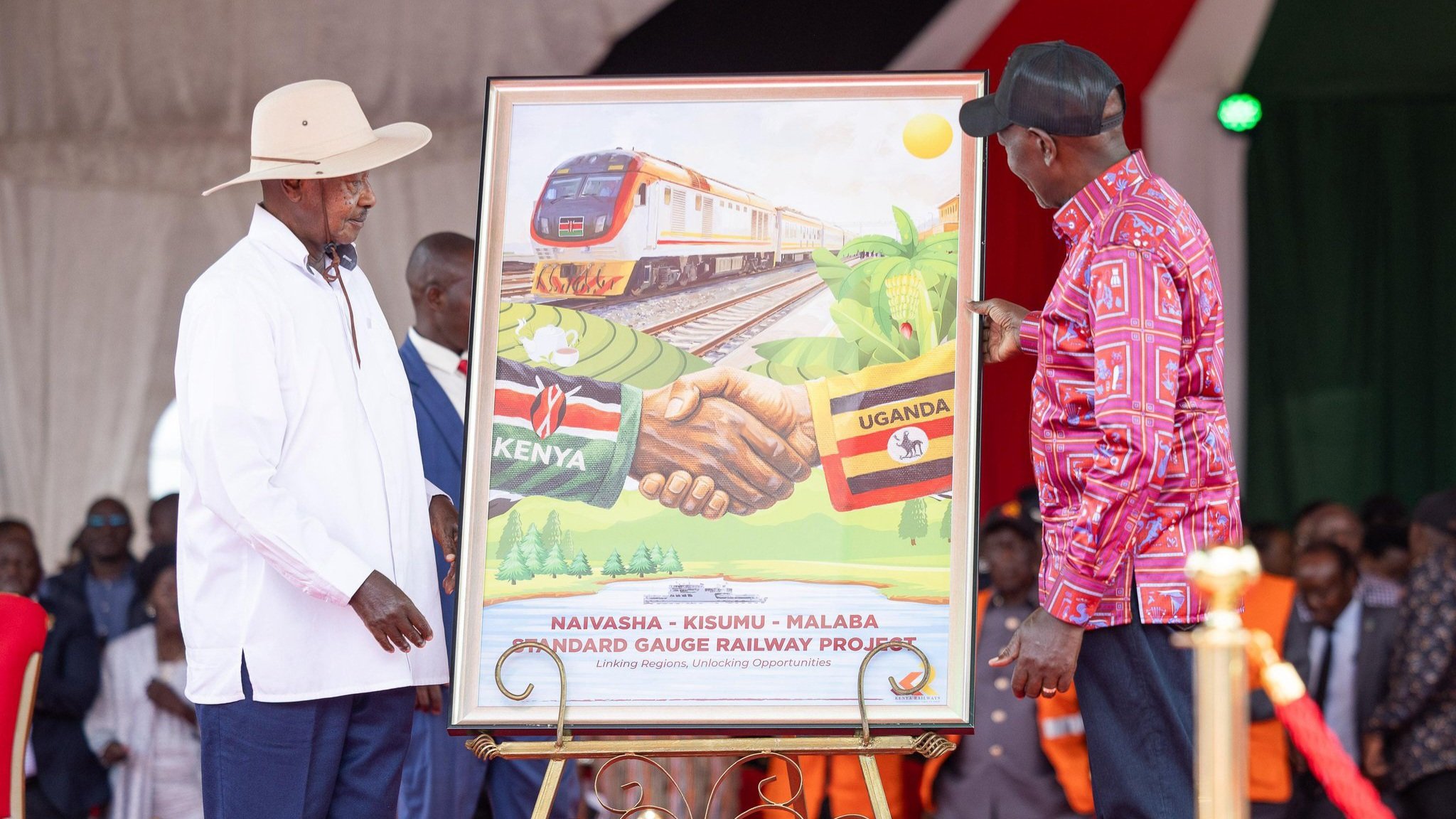 President William Ruto and President Yoweri Museveni standing by a commemorative plaque and a railway track during an infrastructure event.