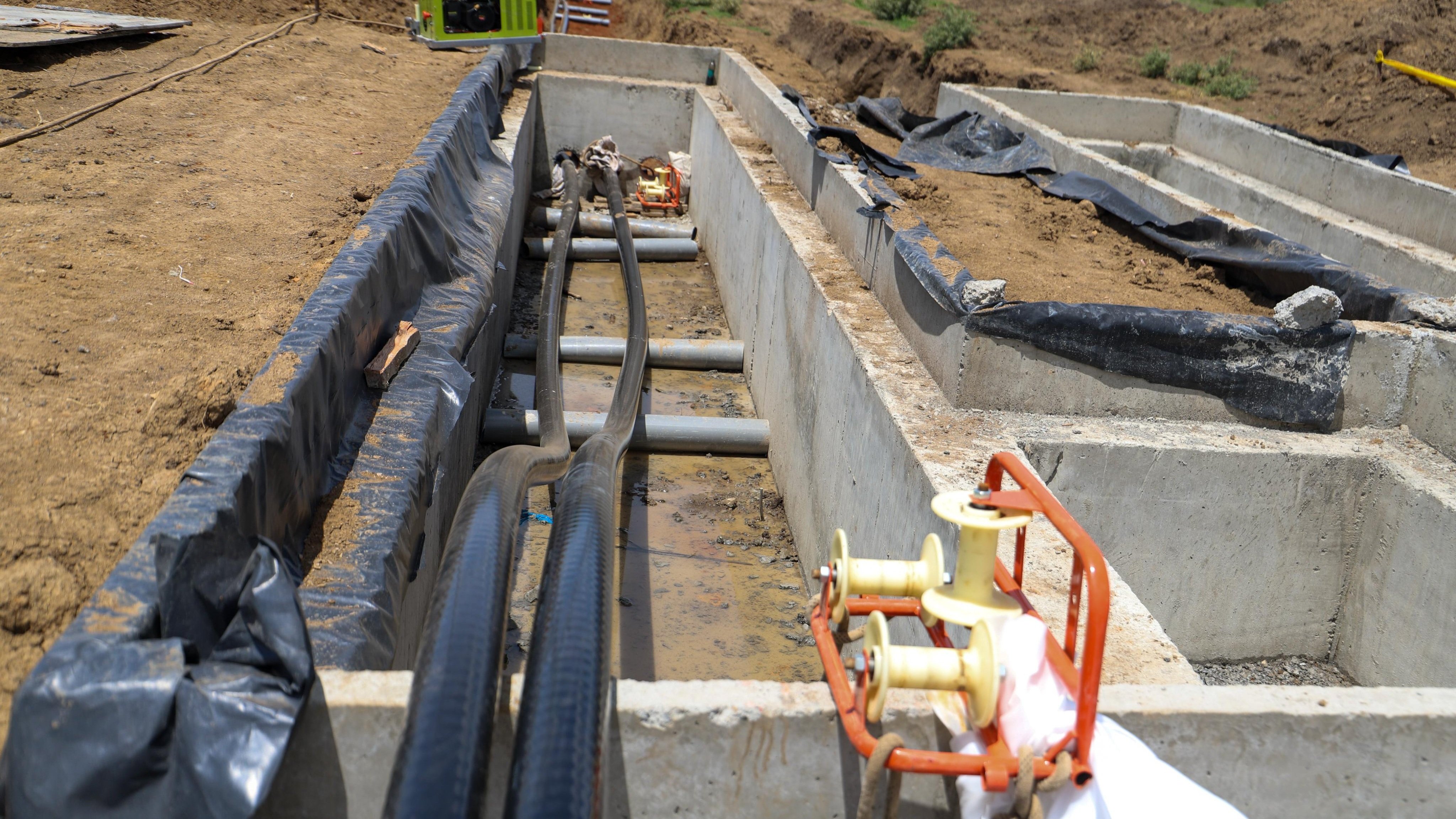 Concrete trench construction site showing underground electrical cable installations and pulling winches.