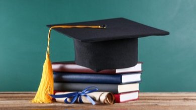 A graduation cap resting on a stack of hardcover academic books with a gold tassel hanging down.