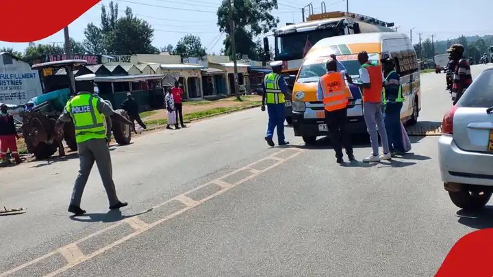 A traffic police officer directs vehicles along a Kenyan highway as a transport compliance vehicle operates in the background.
