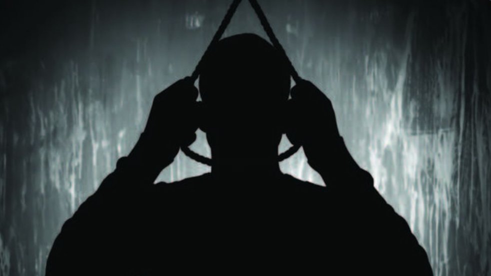 Silhouette of a suicidal man hanging to a rope against a dimly lit background.