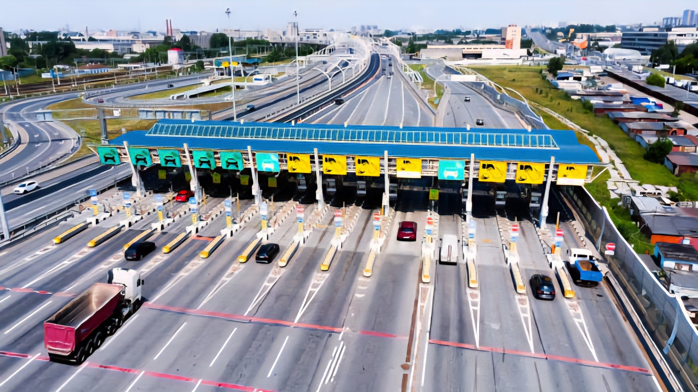 Aerial view of a superhighway showing a toll station, multiple lanes of traffic and greenery on the roadside.