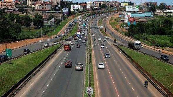 A high-angle view of traffic moving along the multi-lane Thika Superhighway in Nairobi, featuring white and yellow public service matatus.
