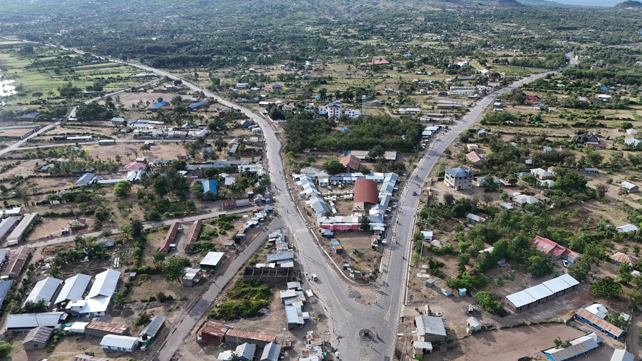 Aerial view of the newly paved Rusinga Island Ring Road showing the bitumen surface winding through a settlement near the shores of Lake Victoria with the Mbita bridge visible in the background.