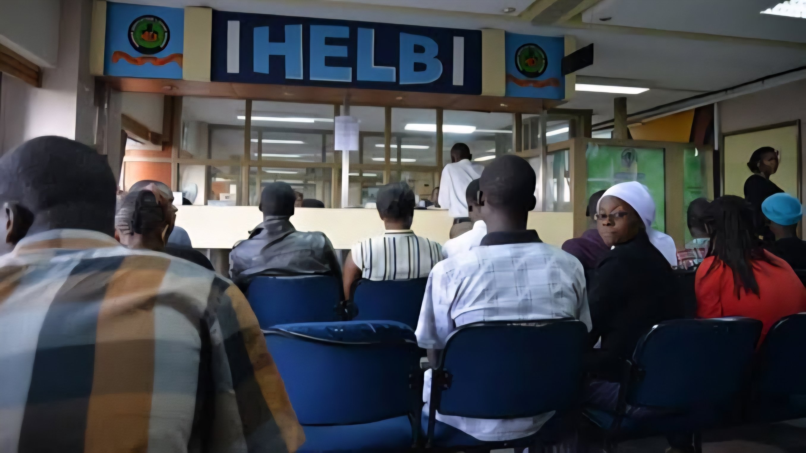 A row of blue chairs occupied by students waiting in the reception lobby area of the Higher Education Loans Board headquarters, with the corporate HELB signage visible above the service counters.