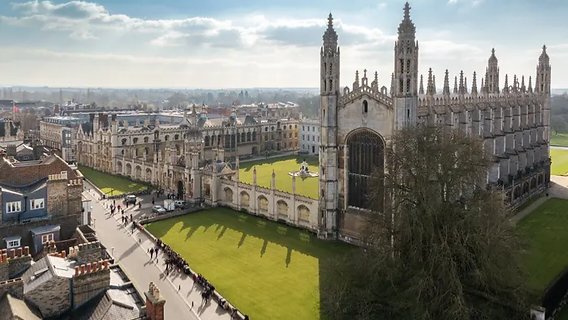 An architectural view of a historic European university campus building with students walking across an open courtyard, referencing file 250115.png.