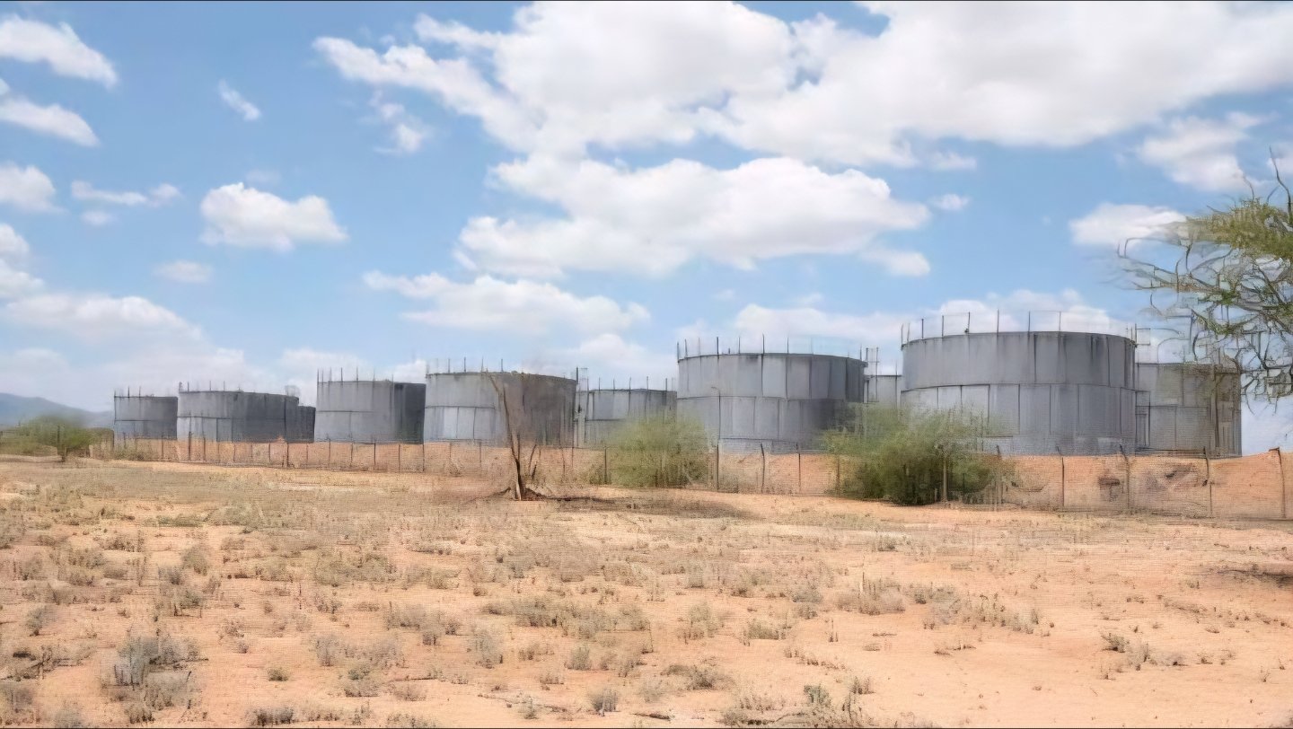 Large silver crude oil storage tanks at the Ngamia 8 site in the Lokichar oil field, Turkana, Kenya, surrounded by arid landscape and a wire fence.