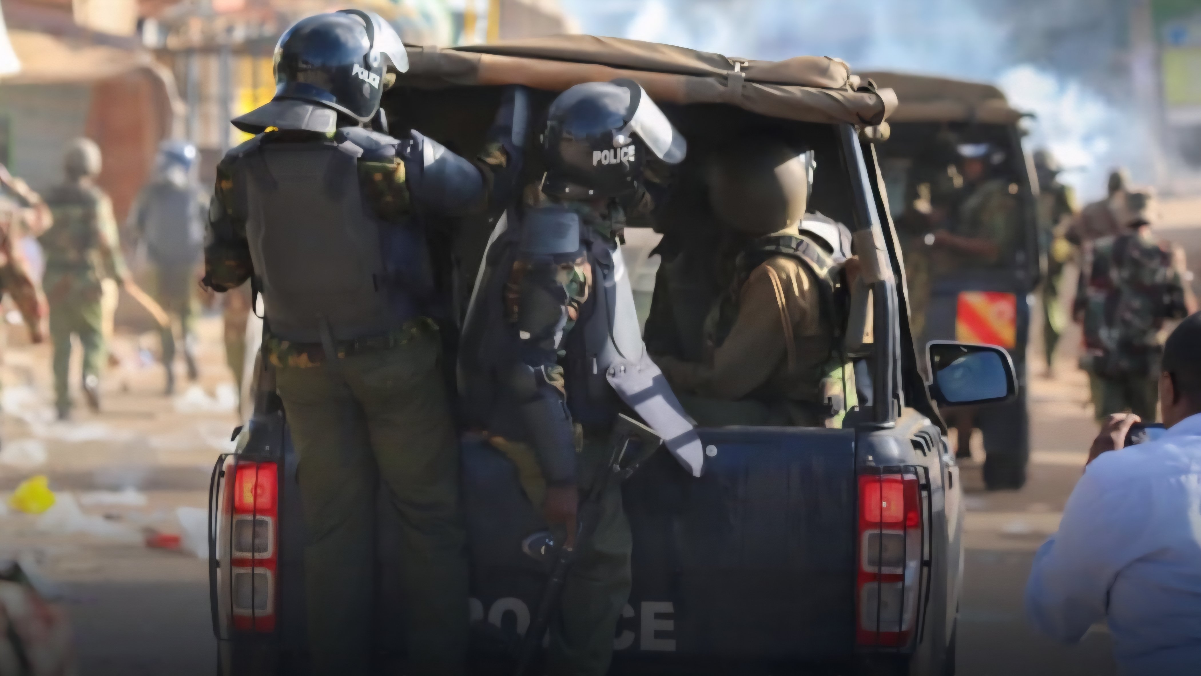 GSU and RDU officers standing in the back of a police vehicle while patrolling a dusty highway in Kenya.