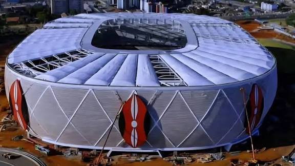 Aerial view of the Talanta Sports City stadium under construction in Nairobi, showing the massive steel roof structure and the Kenyan flag shield.