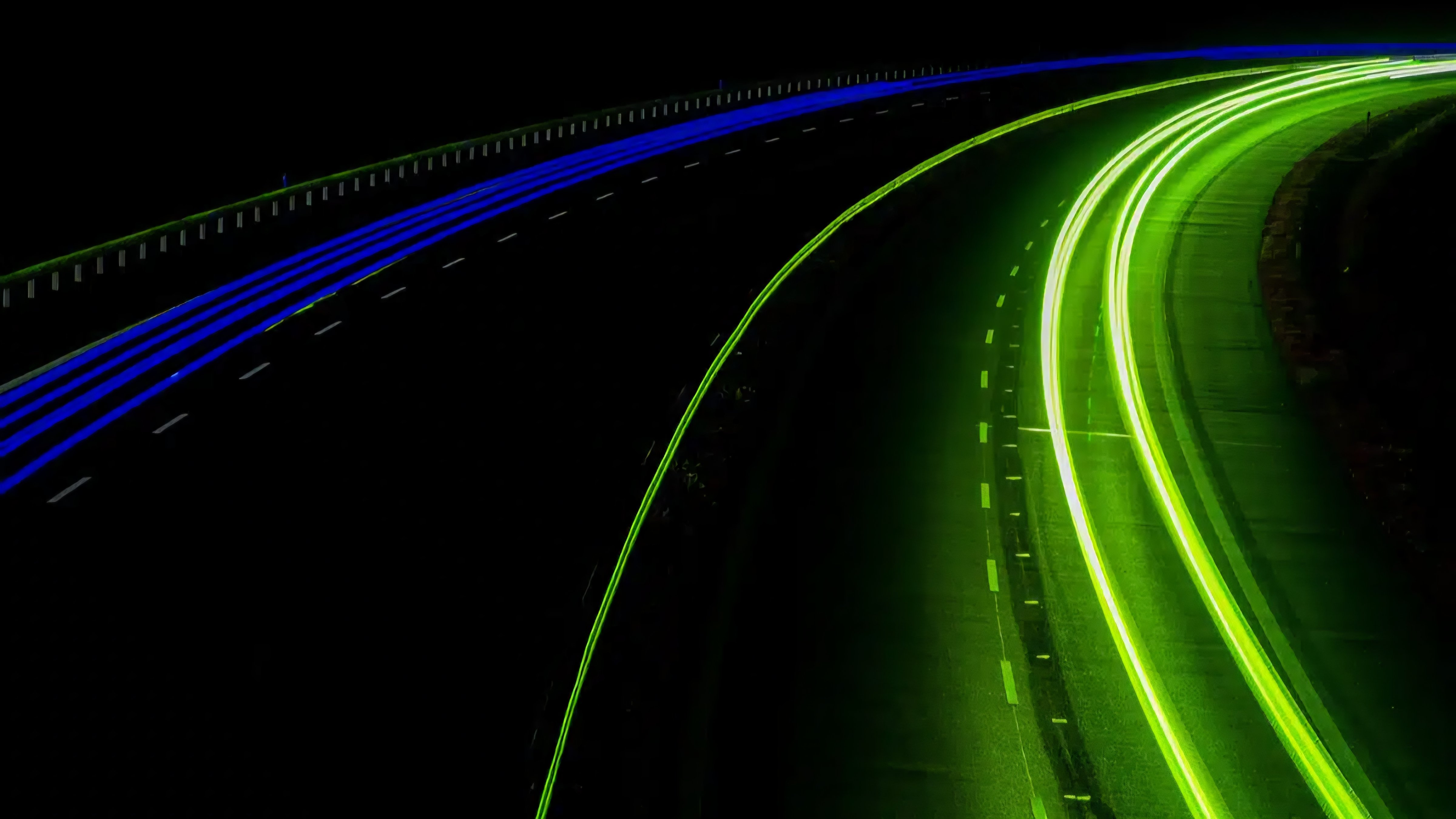 Close up view of glowing green road markings on a dark asphalt surface showing signs of wear and cracking.
