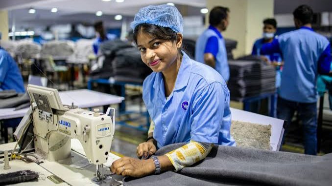 Workers in blue uniforms operating industrial sewing machines inside a garment factory.