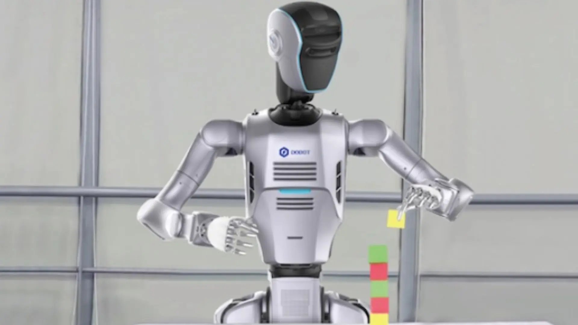 Front view of the silver and white DOBOT LUMO humanoid robot standing indoors against a neutral wall backdrop.
