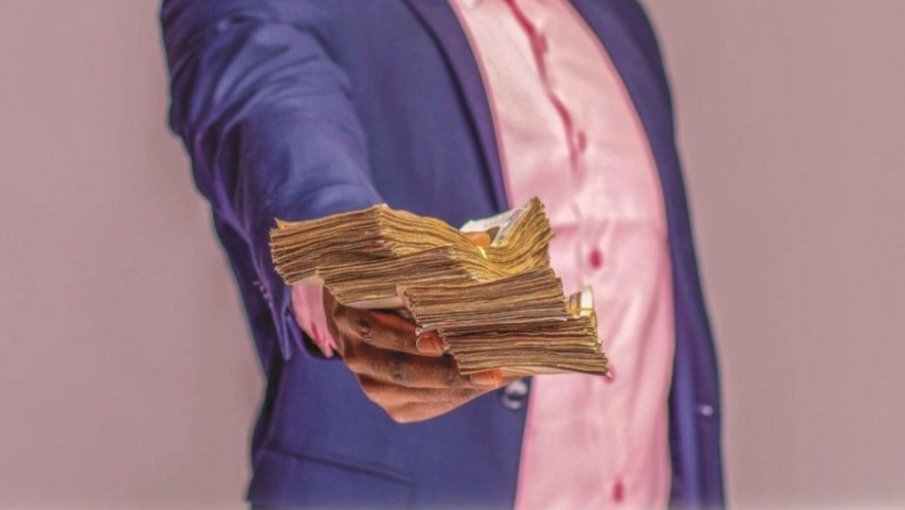 A worker holding a stack of Kenyan currency notes against a business suit.