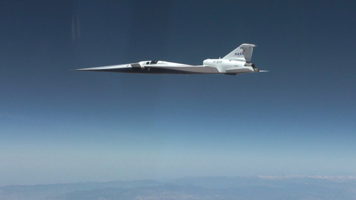 Side view of the white NASA X-59 experimental aircraft flying through a clear blue sky during its first supersonic test flight.