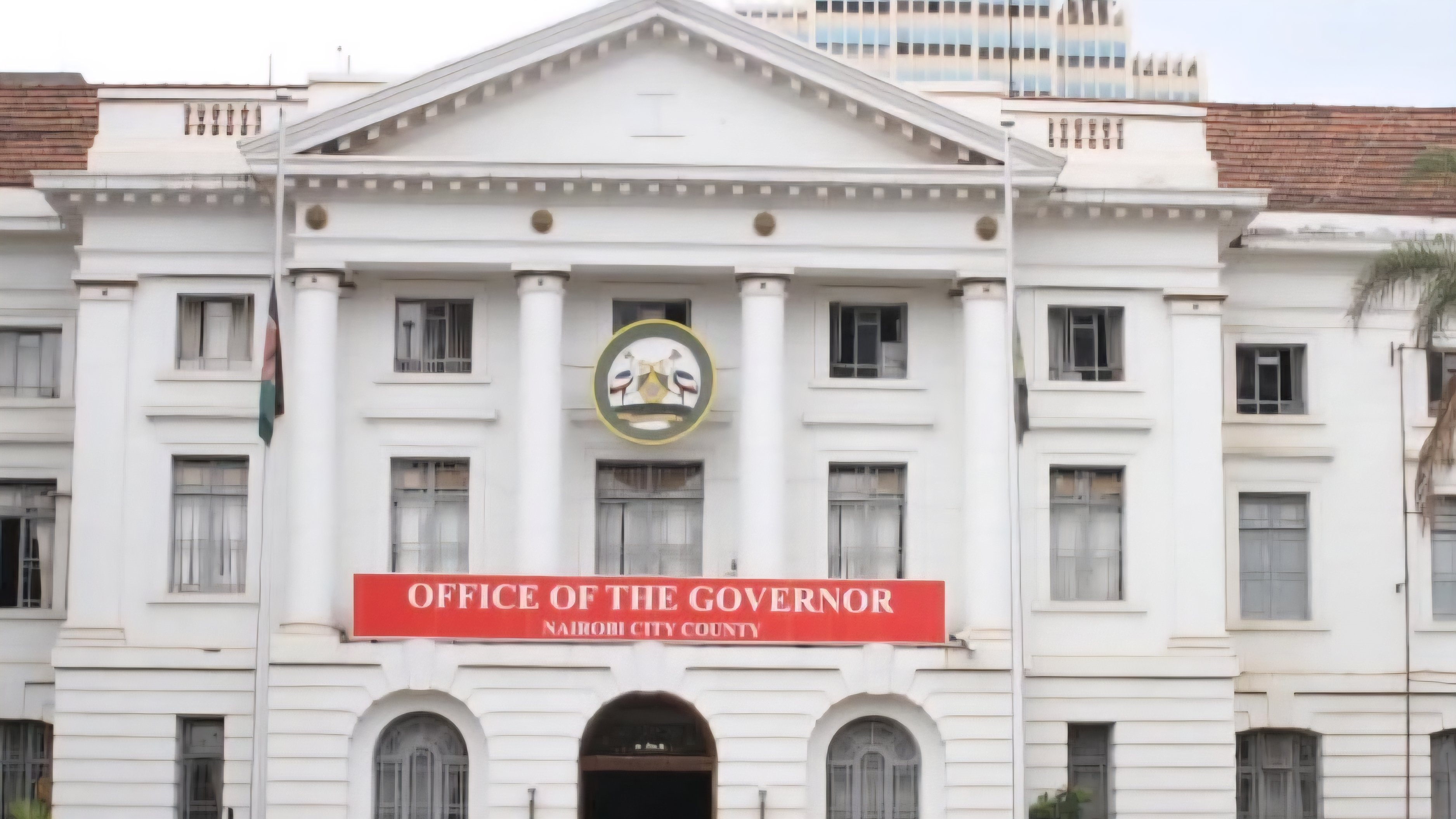 The white colonial-style building of the Nairobi City County Governor's office with a red banner at the entrance.