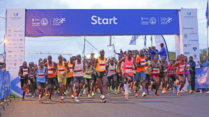 Runners participating in a previous Nairobi Marathon on a major city road, with spectators cheering them on.