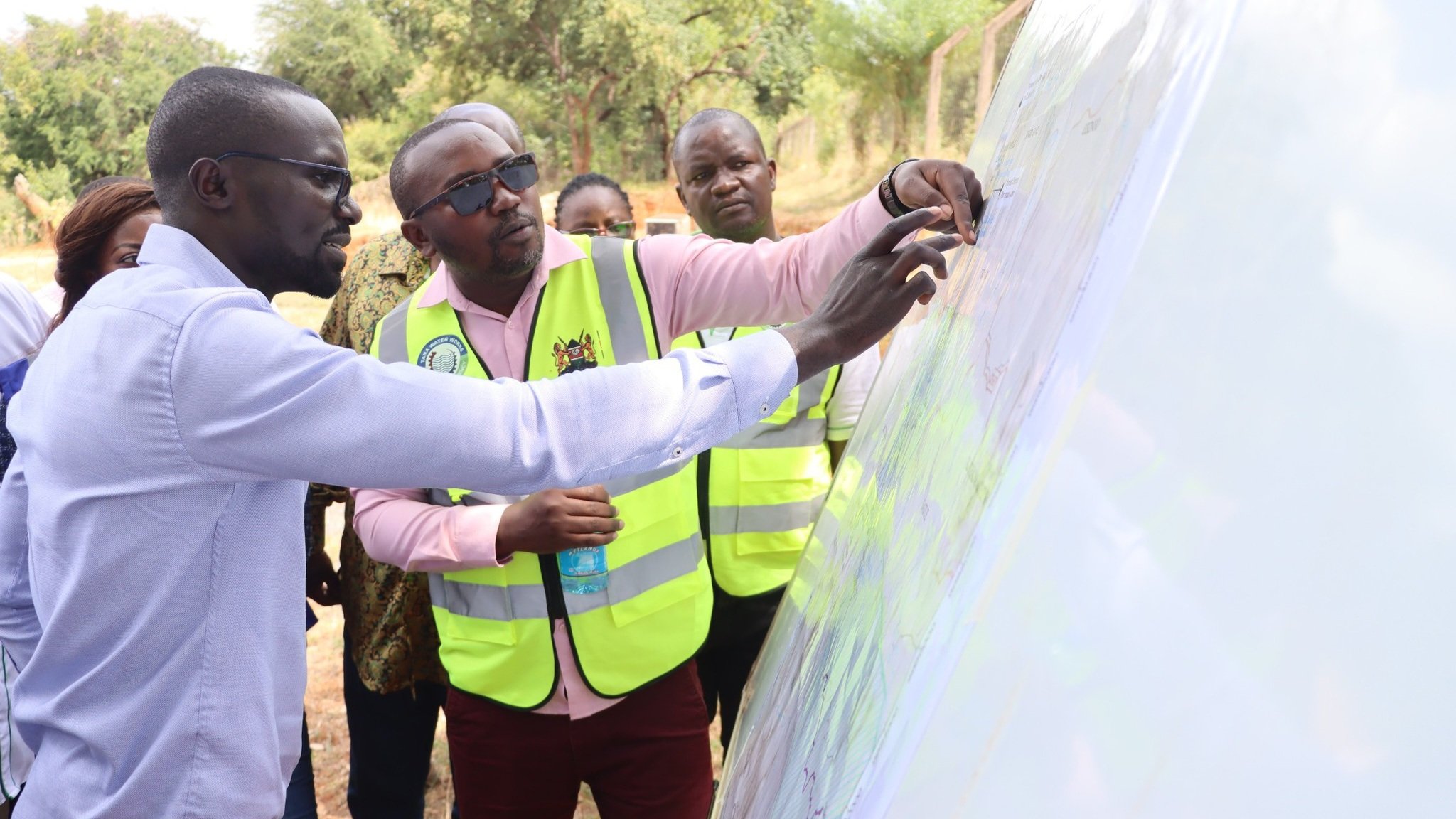 Water Cabinet Secretary Eng. Eric Mugaa inspecting an open excavation trench alongside construction workers in safety helmets and high-visibility vests in Trans Nzoia County.