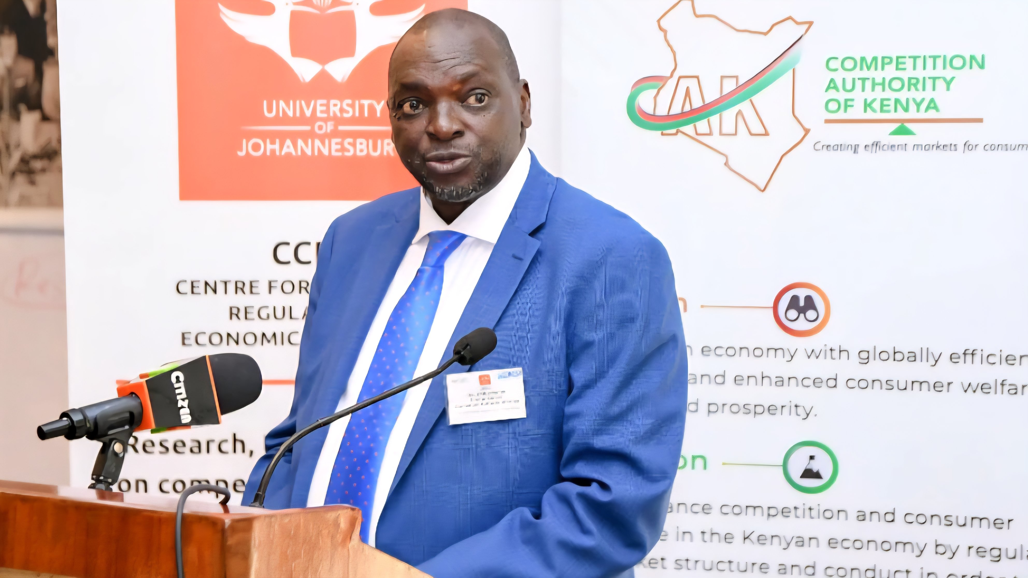 A formal portrait of an official speaking at a podium during a Competition Authority of Kenya event.