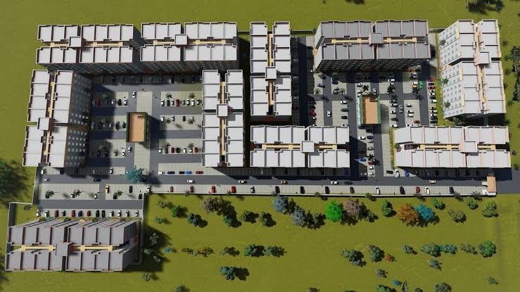 Aerial view of multi-story residential apartment blocks under construction in a dusty landscape with heavy machinery present.