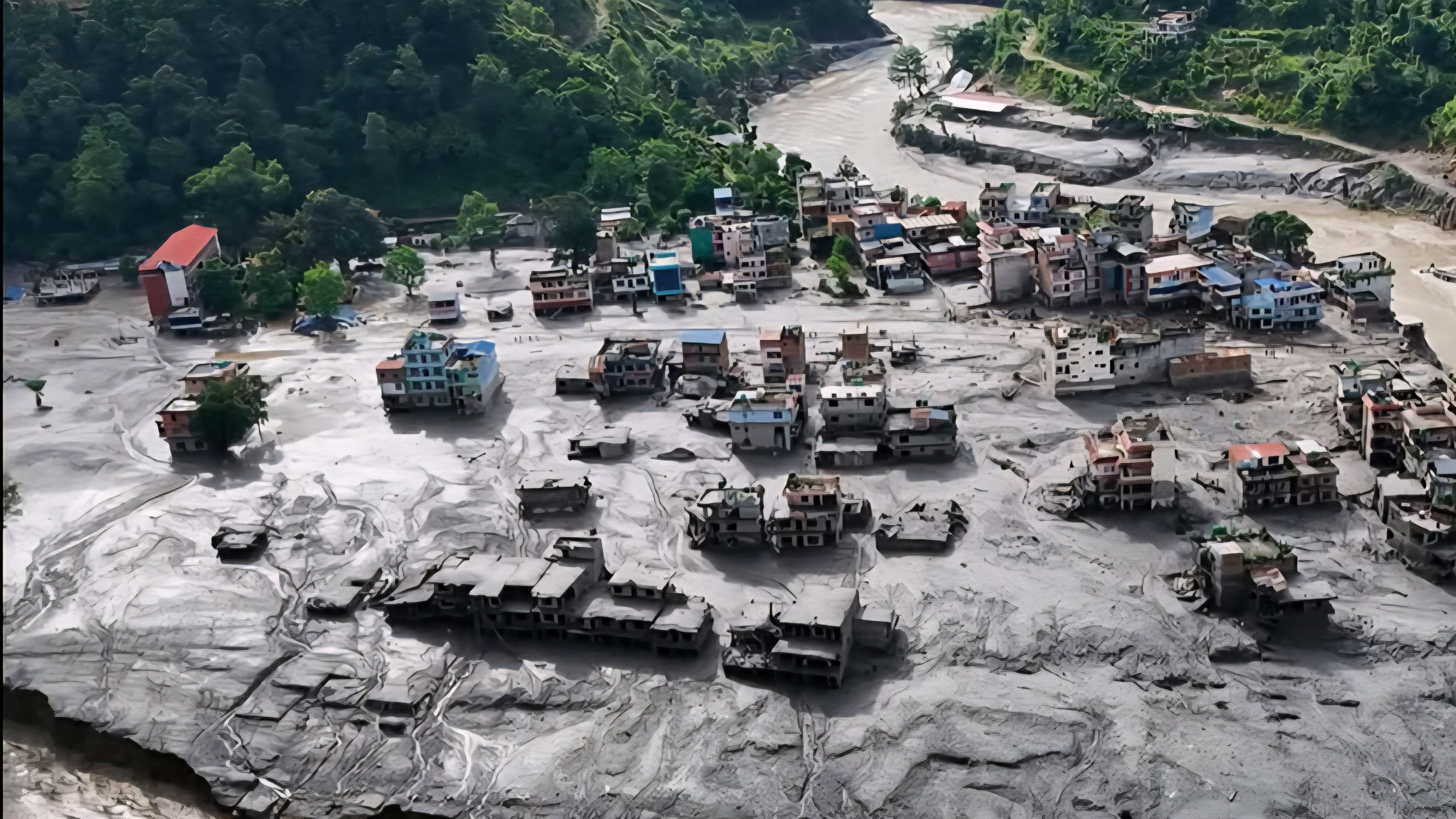 Aerial view of a flood-damaged village along a riverbank covered in thick grey mud and debris on the Nepal-China border.