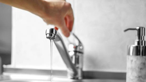 A close-up photograph of a person turning a metallic water tap mounted.