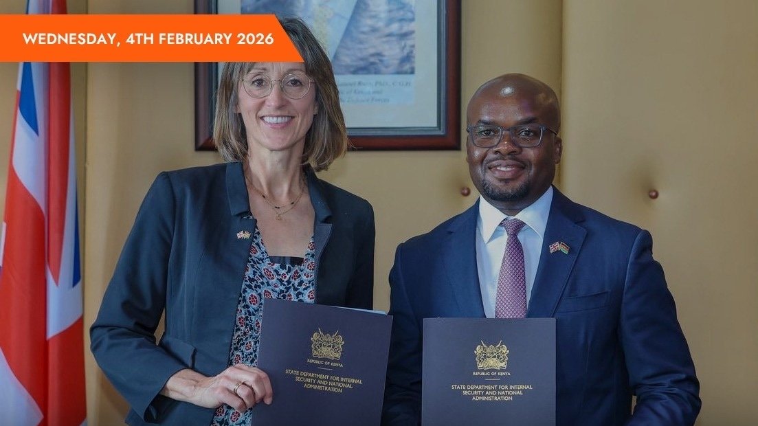Interior Principal Secretary Raymond Omollo and UK Deputy High Commissioner Diana Dalton sign documents at a table with Kenyan and UK flags in the background.