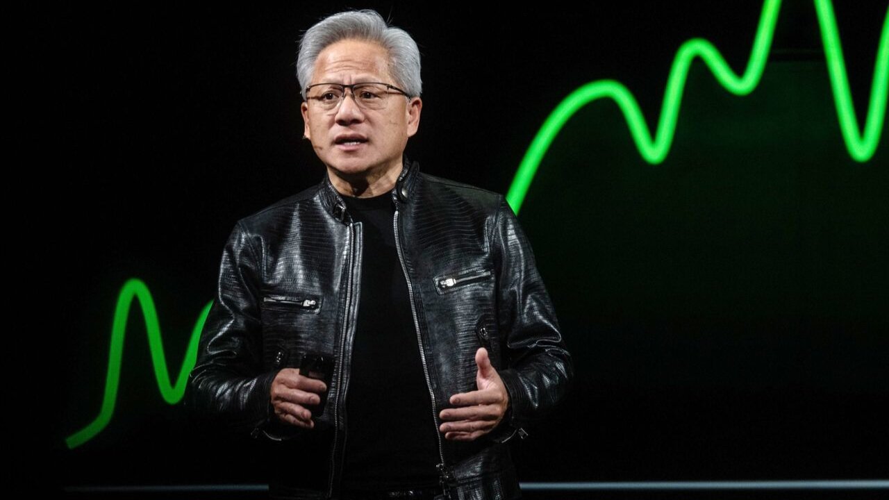 Nvidia chief executive Jensen Huang speaking on stage in a black leather jacket during a keynote presentation.