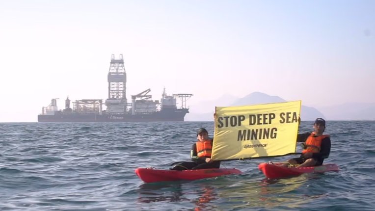 Activists holding a banner in the ocean protesting deep-sea mining near an industrial vessel