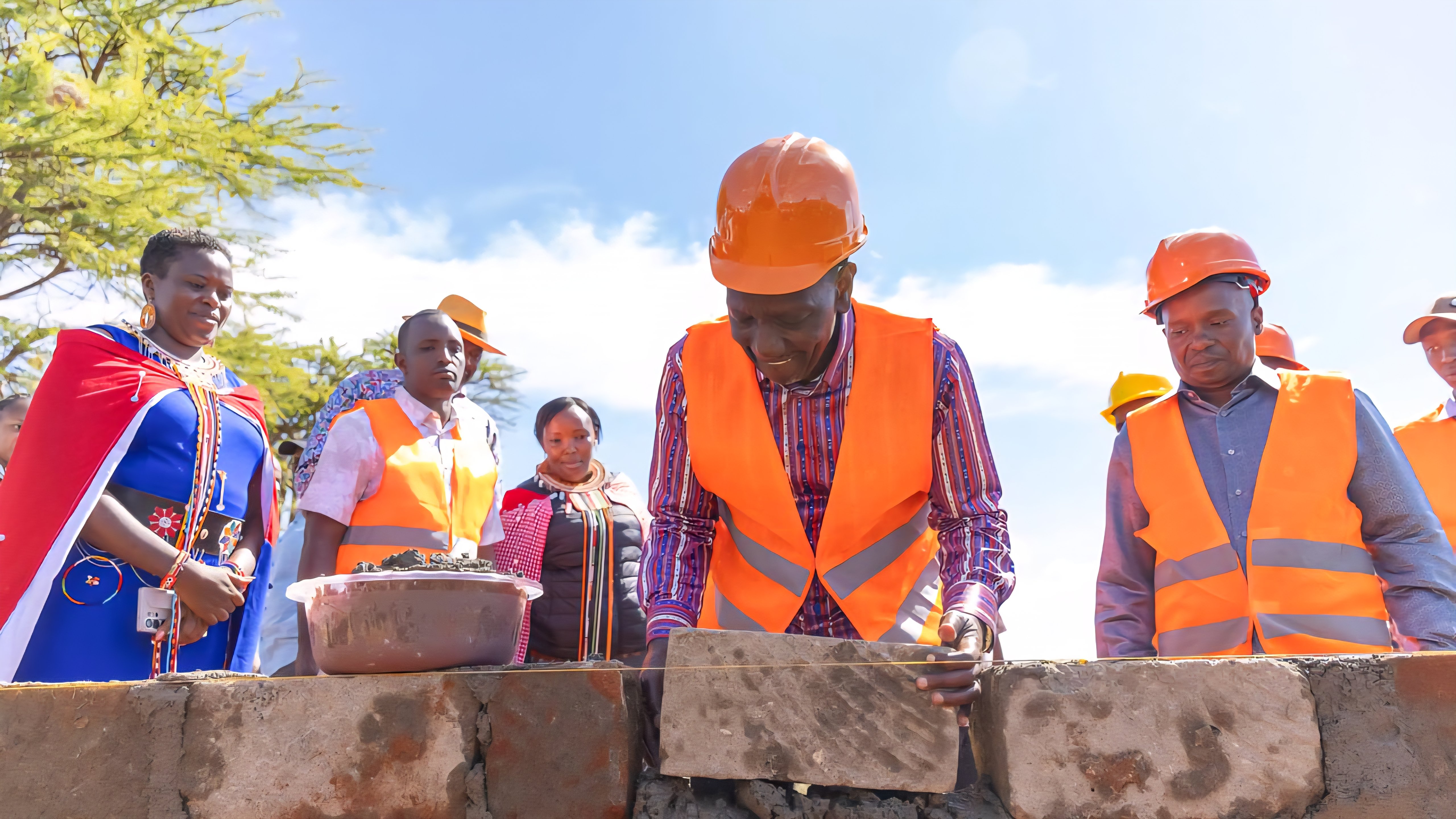 President William Ruto laying a foundation stone for a new building project in Doldol, Laikipia North, surrounded by officials in construction safety gear and a large crowd.