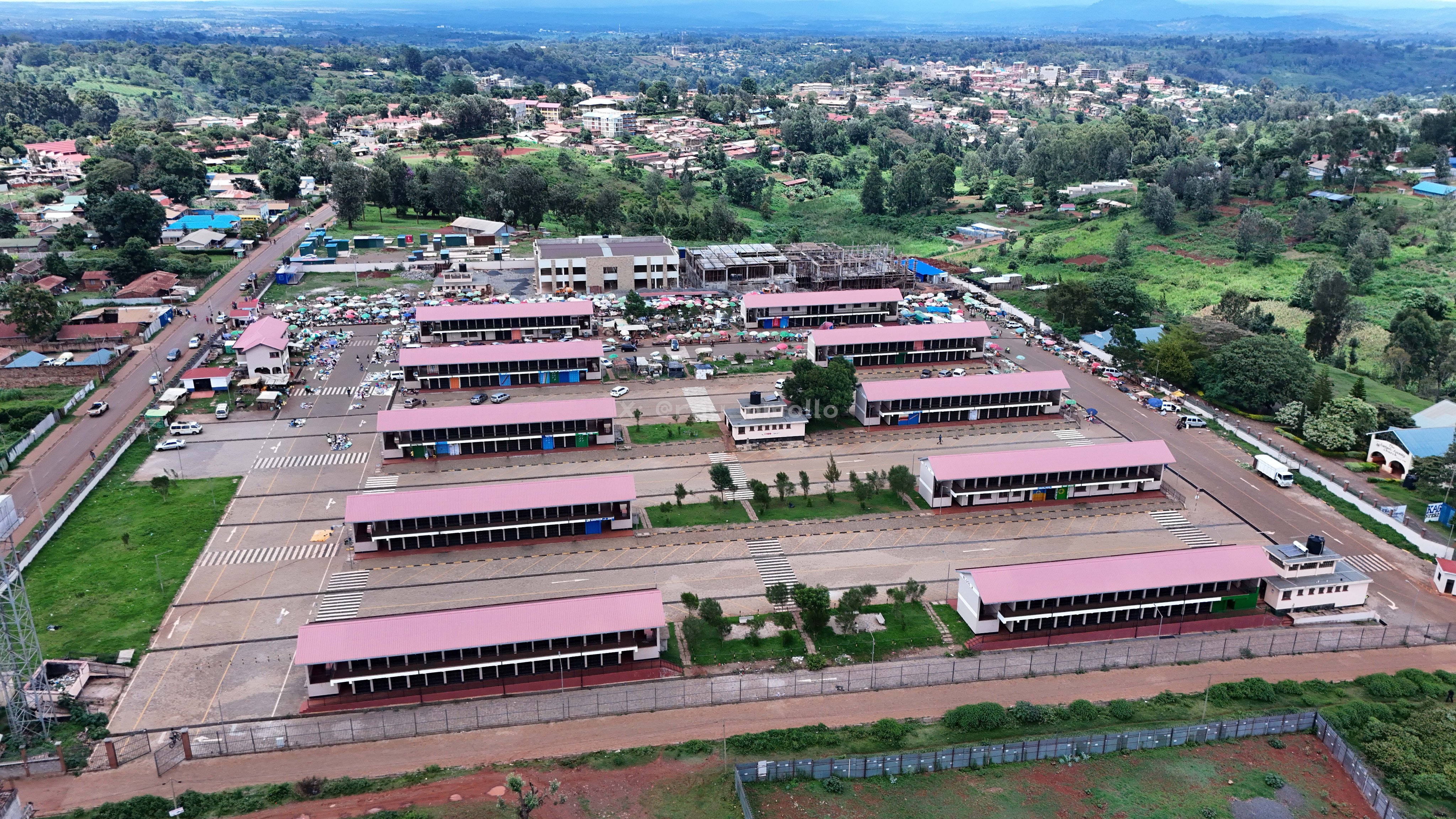 Aerial view of the expansive Field Marshal Muthoni Kirima Modern Market and transport terminus in Nyeri, showing multiple red-roofed stall blocks and organized vehicle bays.