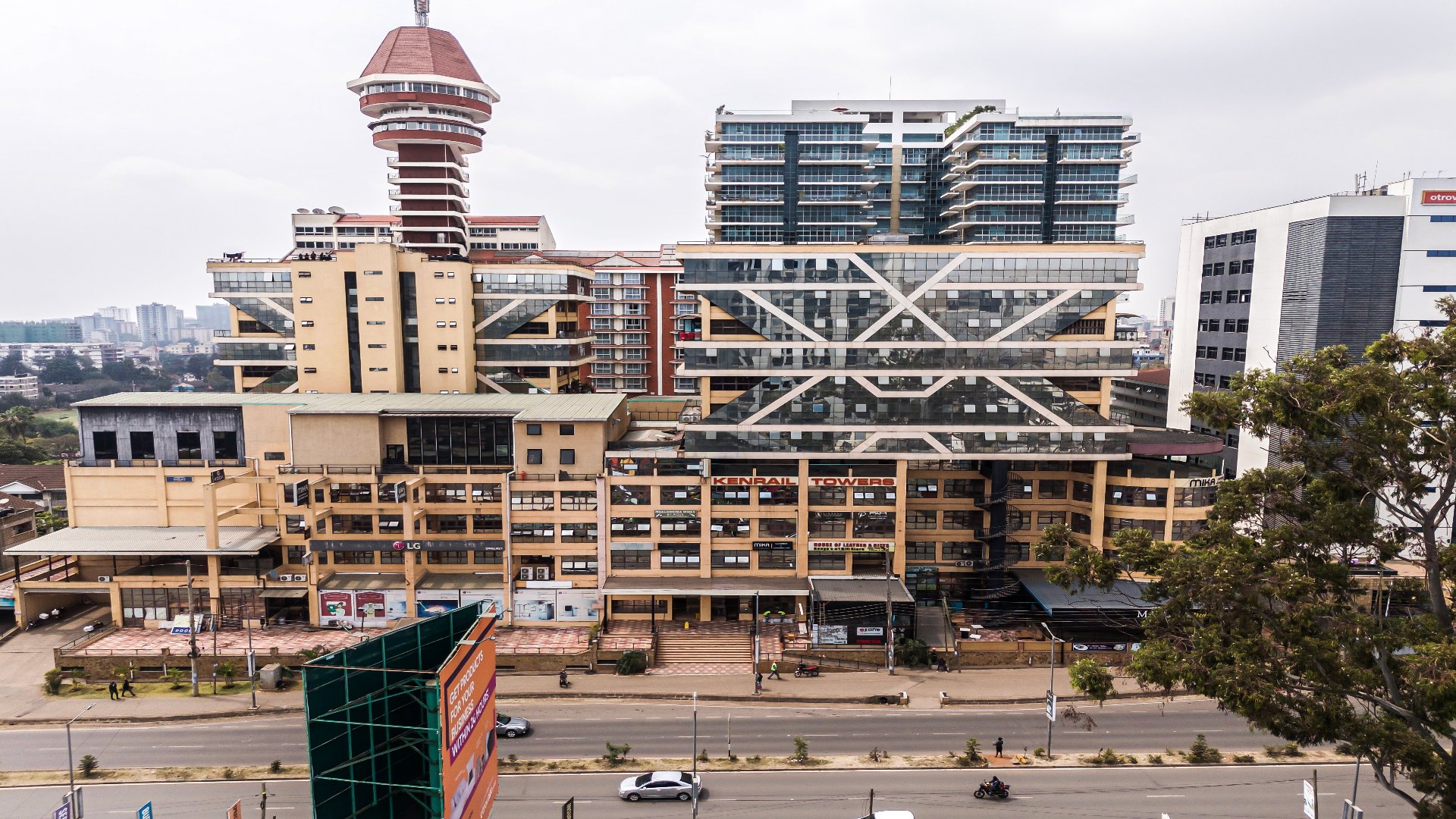 An exterior wide shot of Kenrail Towers in Westlands, Nairobi, showing its distinctive modern architecture with glass facades and structural bracing under a cloudy sky.
