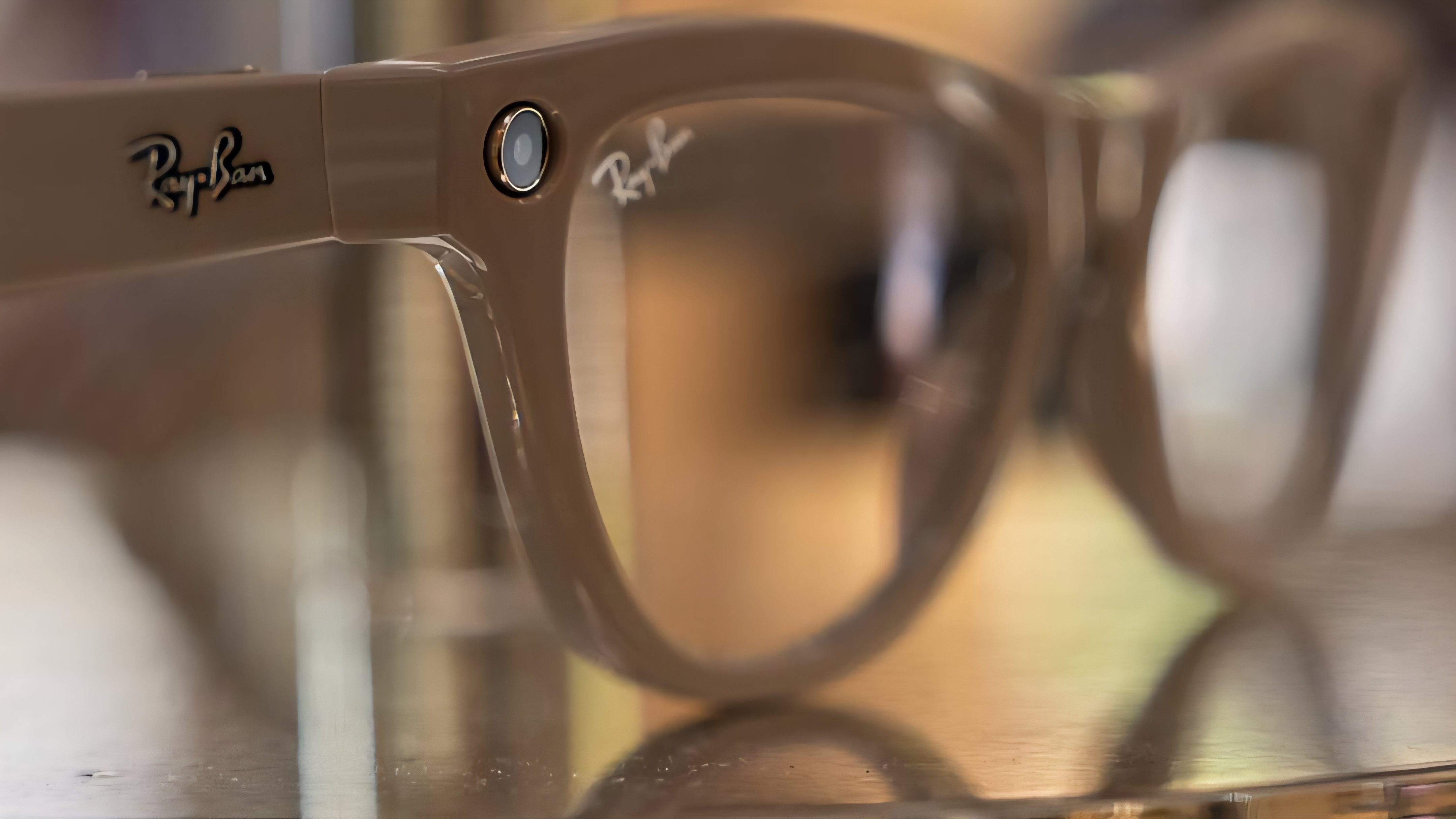 Close-up shot of a pair of transparent brown smart glasses on a metallic surface, showing the subtle camera integration and branding on the frame temple arm.