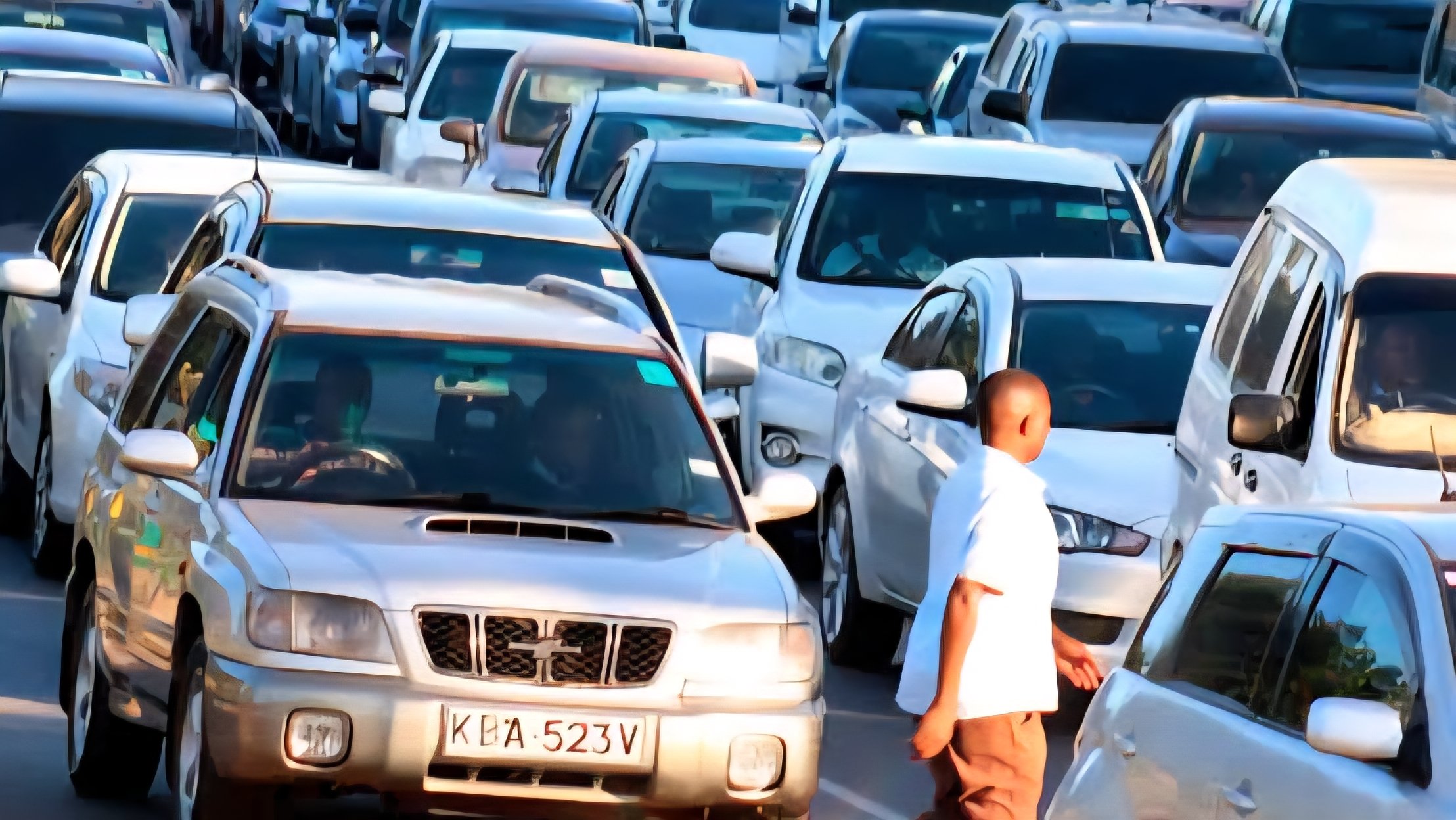 Heavy traffic congestion consisting of white vans and private cars on a multi-lane highway in Nairobi, Kenya.