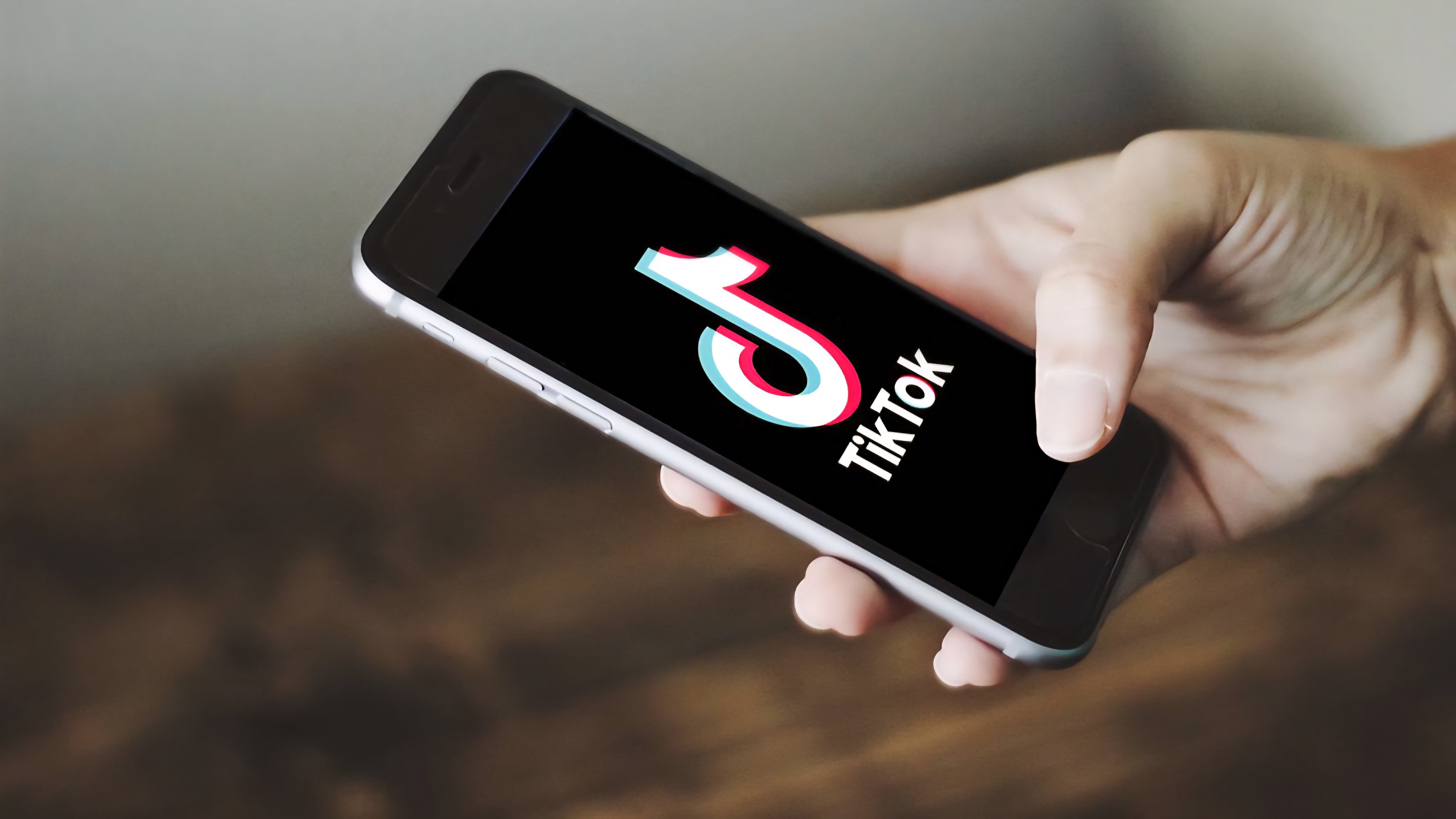 A person holding a smartphone showing the TikTok logo on a purple-lit background.