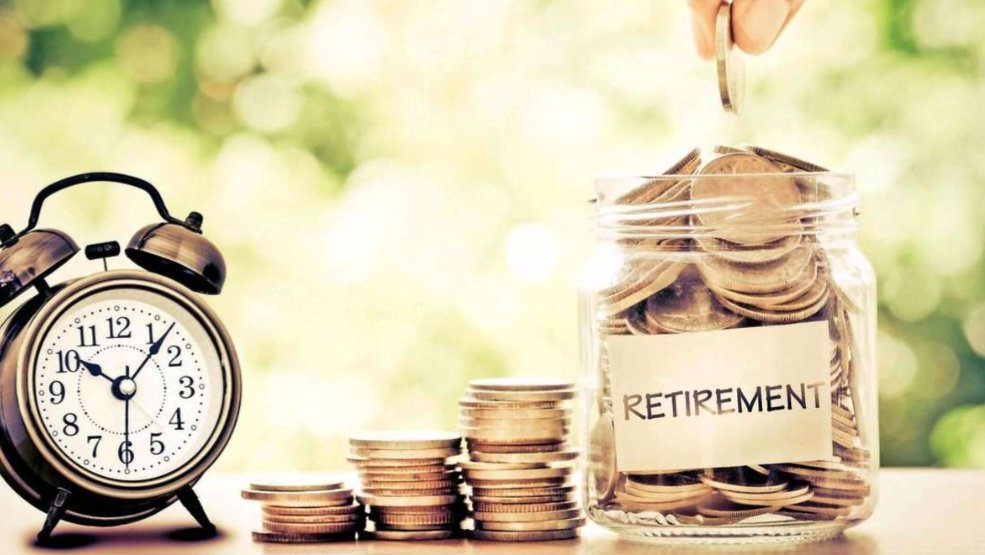 A glass jar filled with coins next to an alarm clock and a wooden card reading RETIREMENT.
