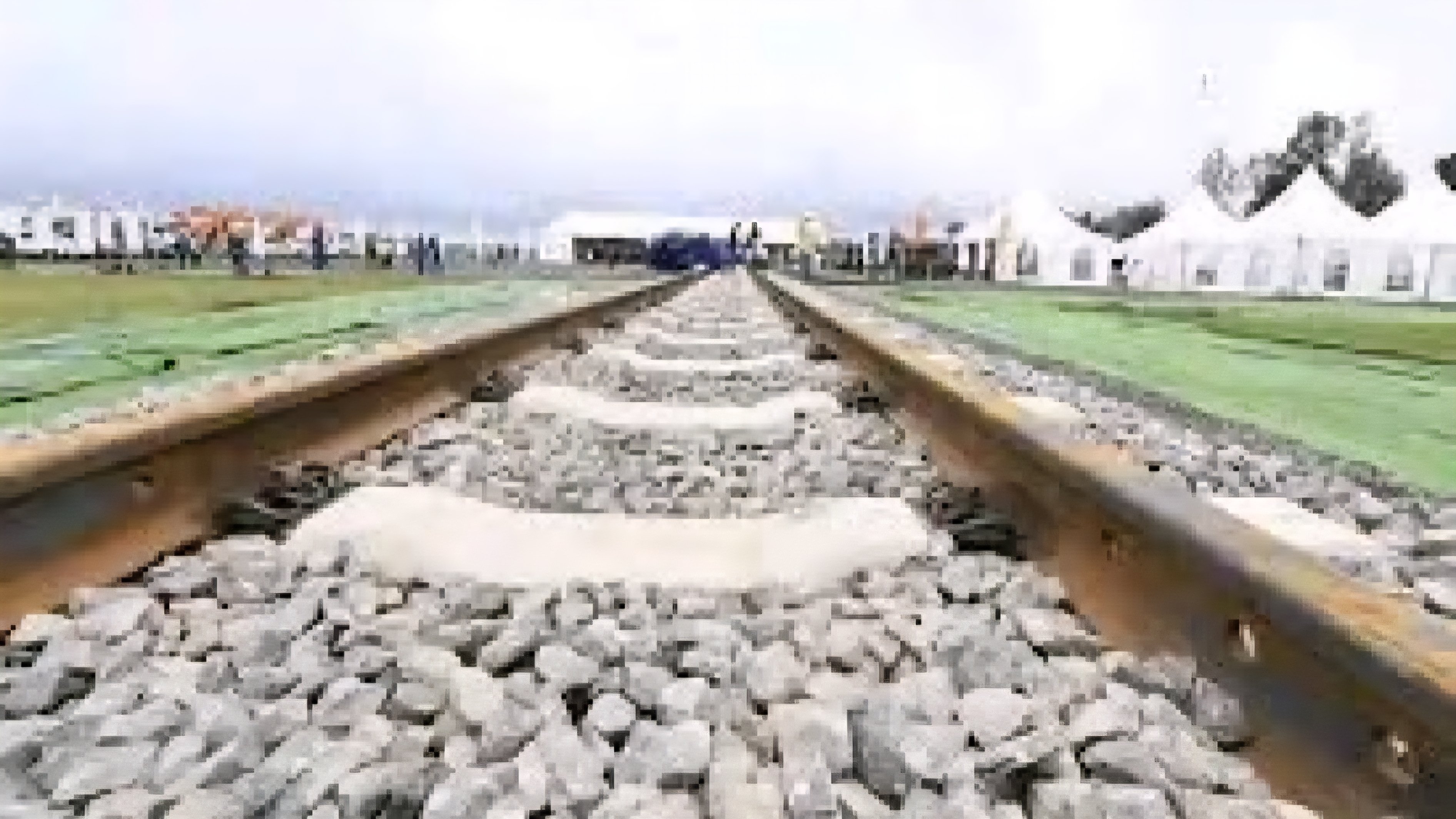 A low-angle perspective of a single-track railway line leading toward a distant construction site with white tents.