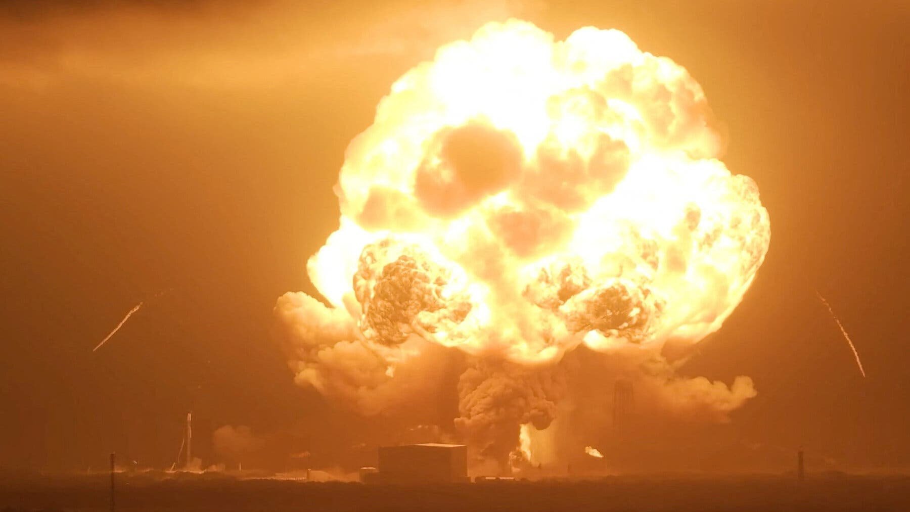 A close-up view of a massive orange and white fireball billowing into the night sky following a rocket explosion on a launchpad.