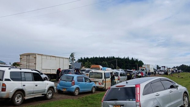 A line of vehicles moving through a traffic checkpoint on a Kenyan highway with police officers directing flow.