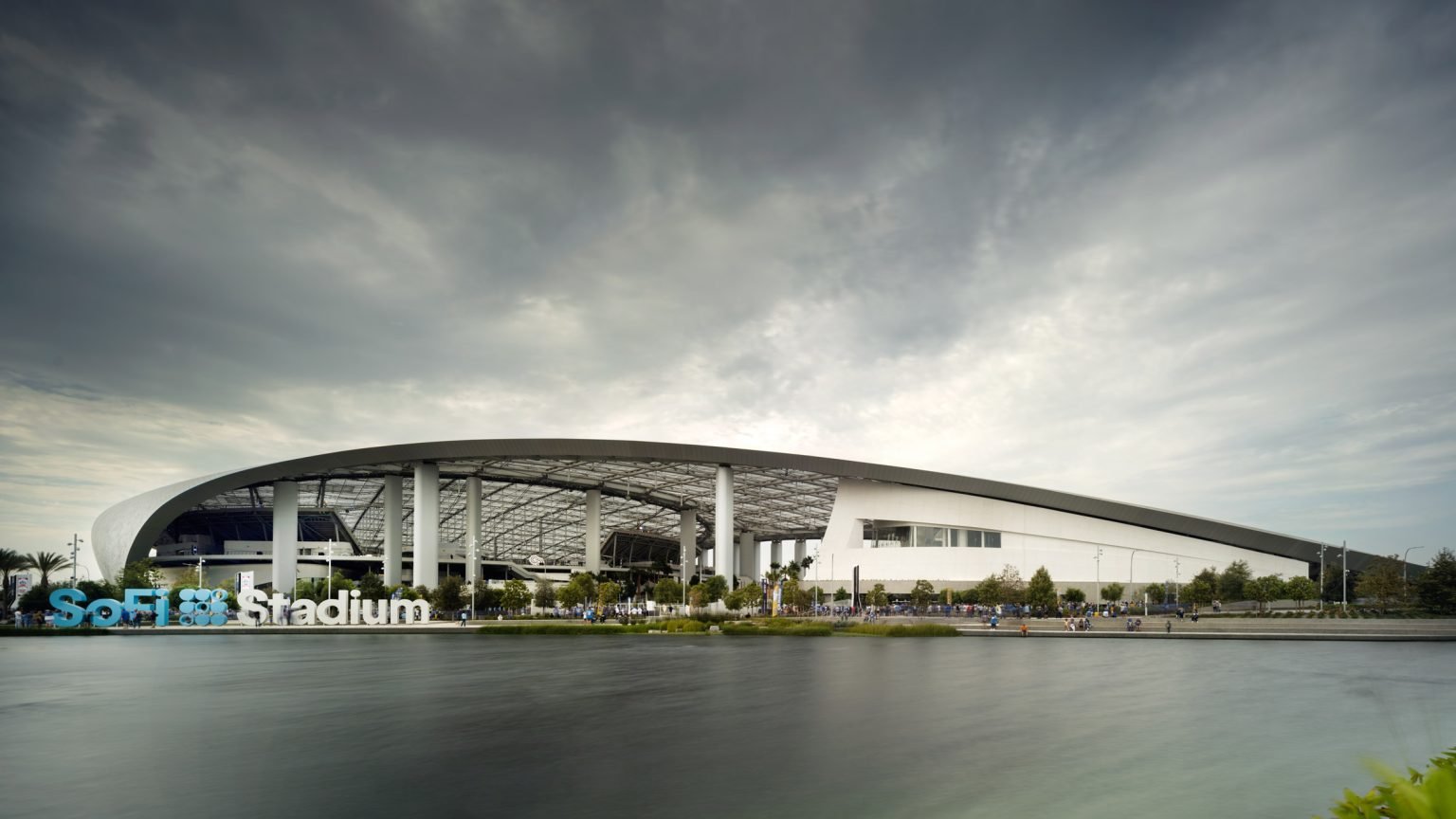 Wide-angle exterior view of SoFi Stadium in California showing its swooping roof canopy and front public plaza.