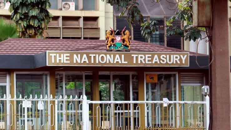 Exterior sign reading The National Treasury mounted on a building entryway with the Kenyan coat of arms above the lettering behind a white metal fence.