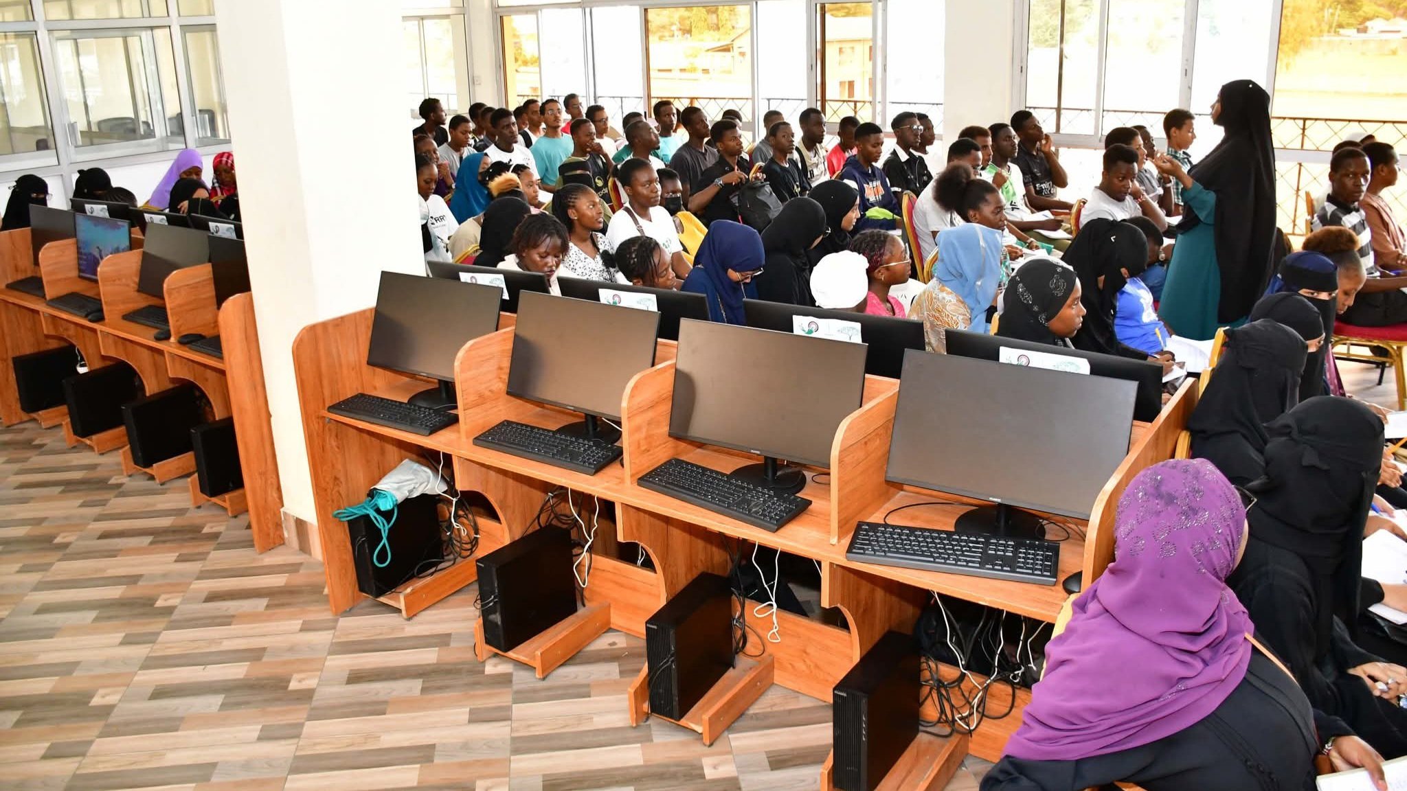 A row of modern computer workstations inside a brightly lit digital laboratory with participants engaged in training sessions.