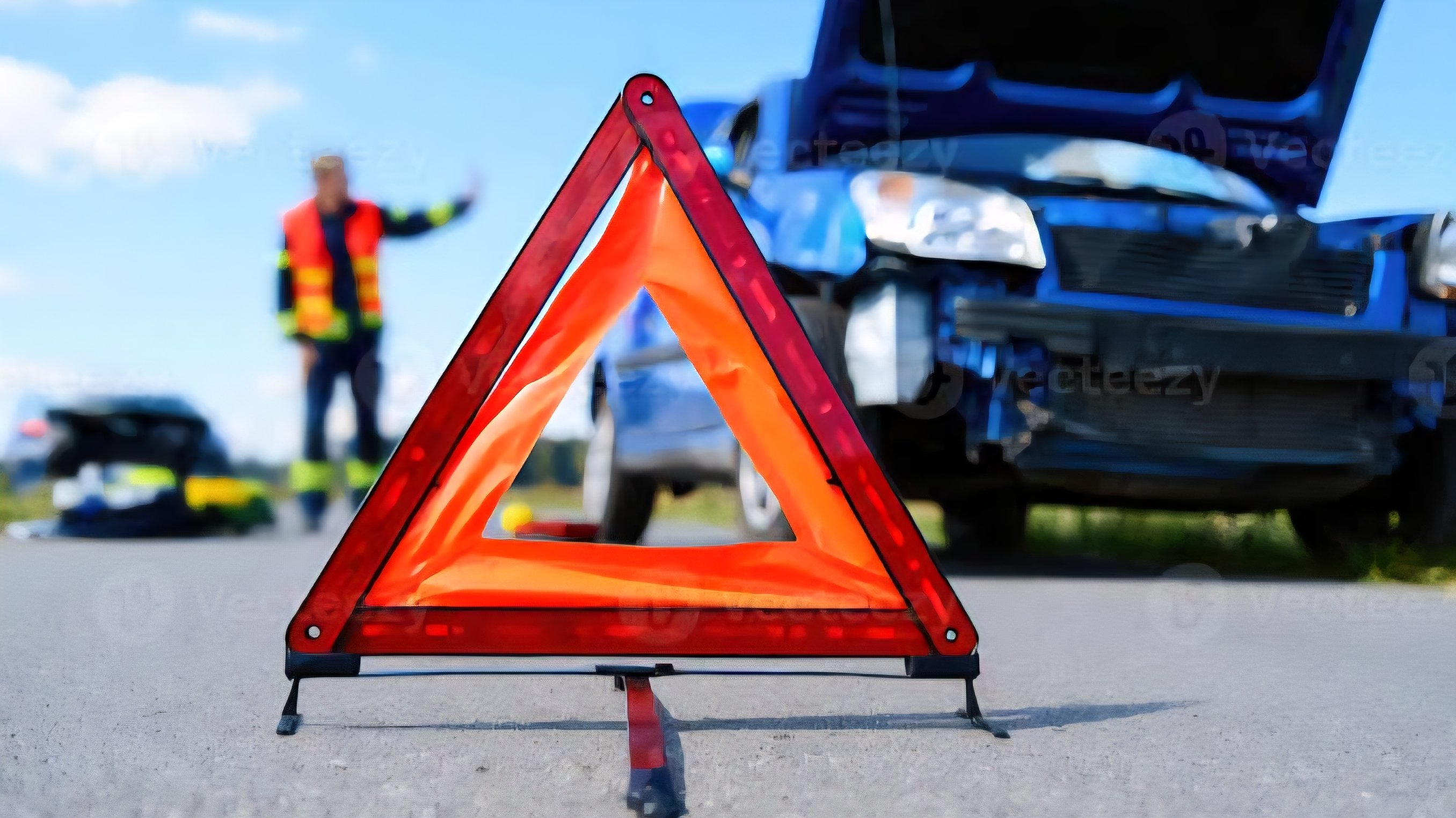 Red and white warning triangle sign with the word Accident placed on a road with traffic cones in the background.