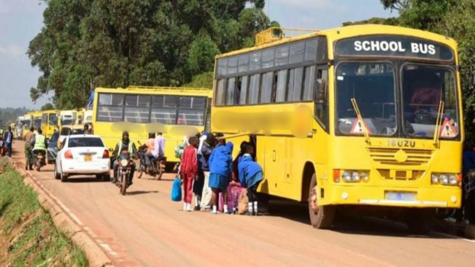 A yellow school bus parked at a bus stop with students boarding under the supervision of a school official.