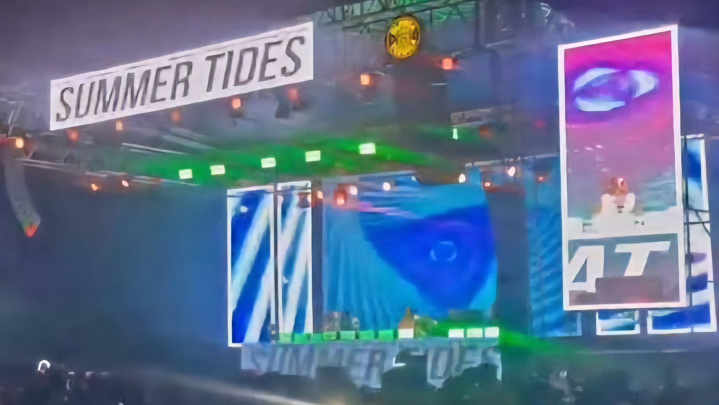 A large outdoor entertainment stage with bright pink screens and the words Summer Tides illuminated during a night concert.